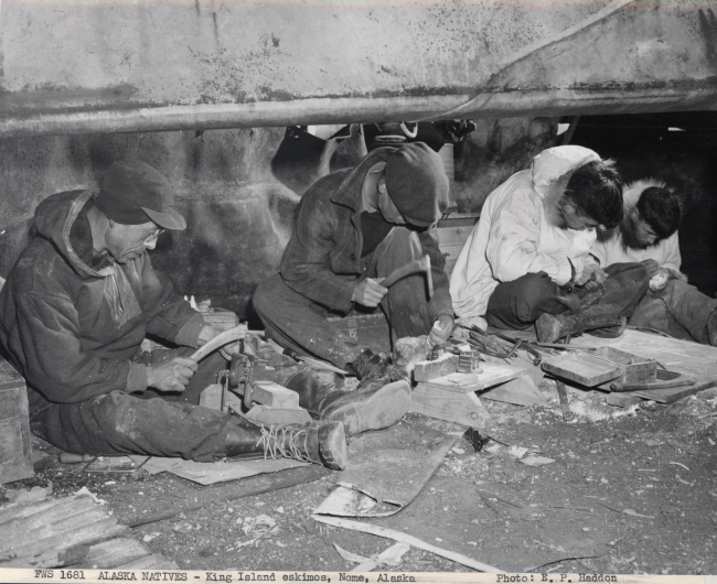 King Islanders carving ivory beneath the skin-covered umiaks on the beach atNome where they have a summer camp