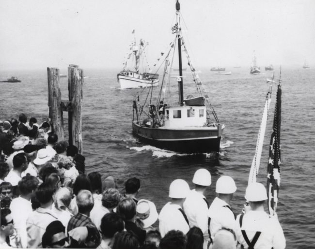 Fishing vessels passing pier and honor guard during Annual Blessing of the Fleet