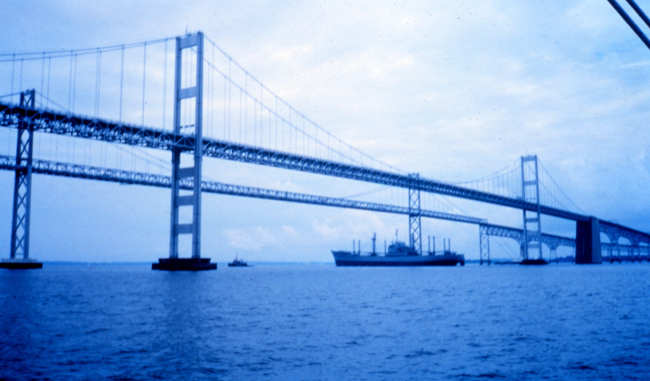 A tugboat tows an old freighter down the bay and under the Chesapeake Bay Bridge