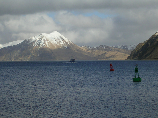 A volcanic cone, buoys, and a fishing vessel complete a Dutch Harbor scene