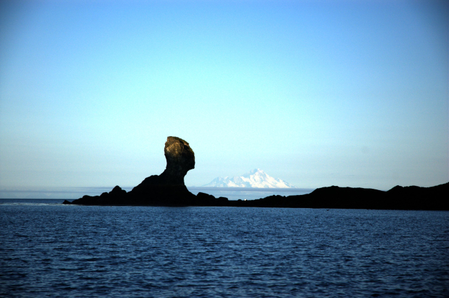 Illiamna Volcano seen to the right of a mushroom rock across Cook Inlet from Kachemak Bay