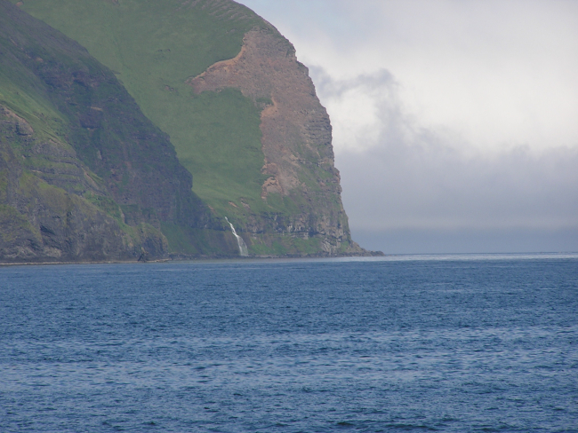 A waterfall rushing to the sea between impressive Aleutian cliffs