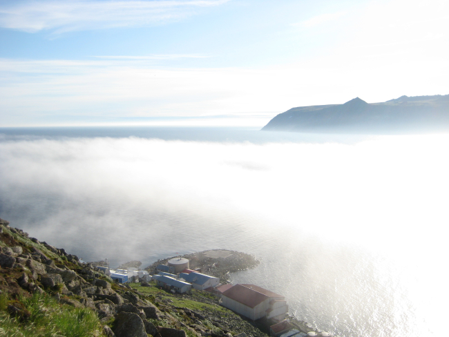 Looking over the village at Little Diomede Island to the fog shrouded straitbetween Little Diomede and Big Diomede Islands