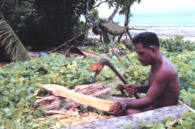 Native Micronesian making a paddle with an adze for his outrigger canoe