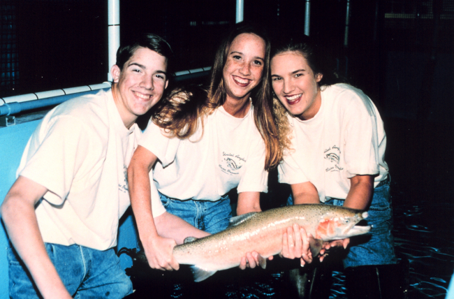 Three students pose with a steelhead trout at their fish hatchery