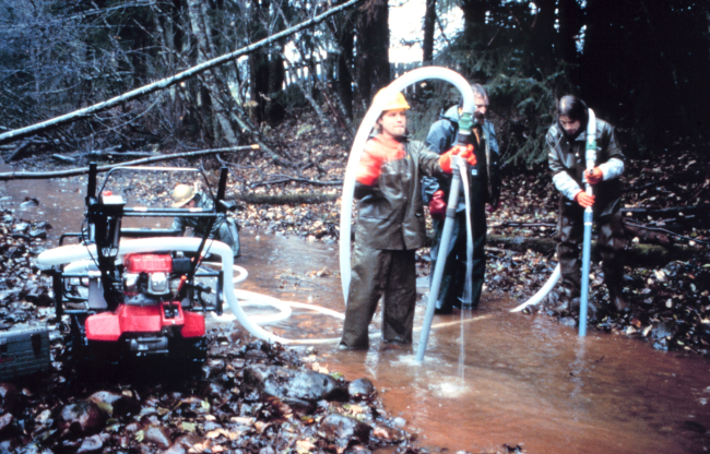 Three workers use the pump used to loosen sand and gravel at Duck Creek
