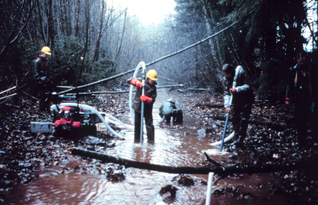 Three men in the river operate the pump