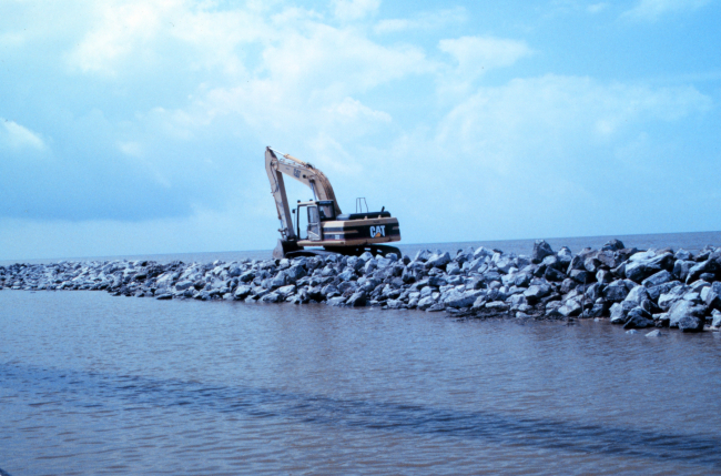 A view from the Mobile Canal of a back hoe placing rock at the narrow beach