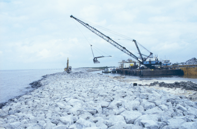 A barge-mounted crane loads rock which will be placed to stabilize shorelineerosion