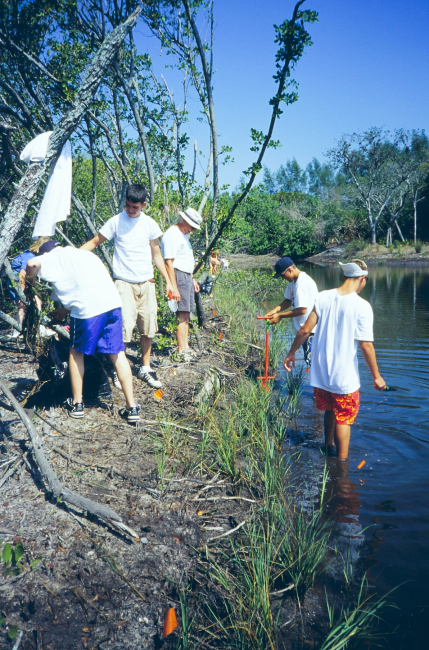 A student at the water's edge is using a dibble bar