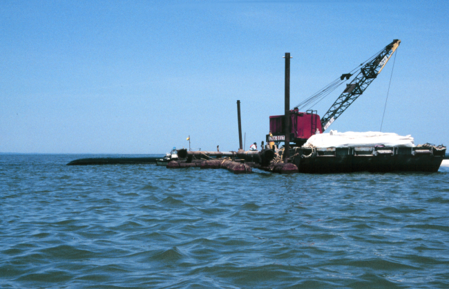 A barge with a crane is filling a geotube, in the background of the image