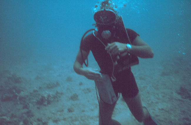 A diver equipped with underwater tape recorder, wetsuit, watch for determining dive time