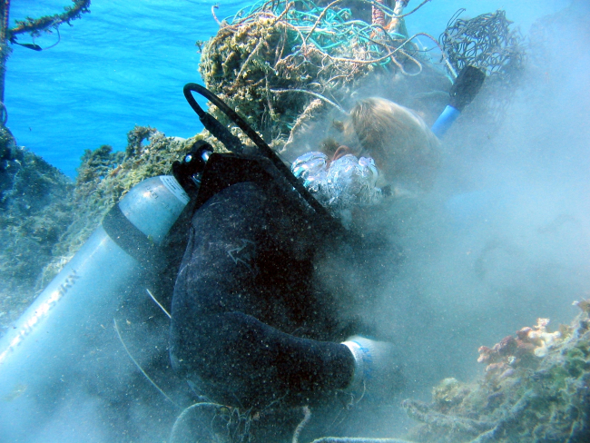 Scuba diver cutting derelict net material free prior to floating free portionto surface