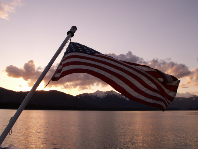 Old Glory waving from the stern of the RAINIER at sunset