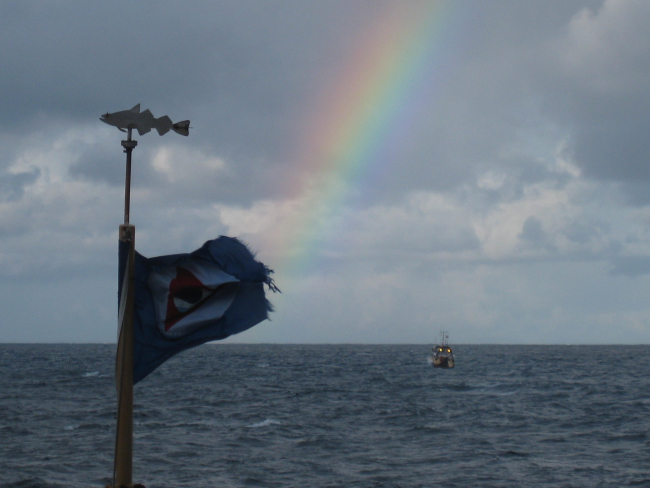 A somewhat wind-torn and tattered NOAA flag, rainbow, and small sterntrawler