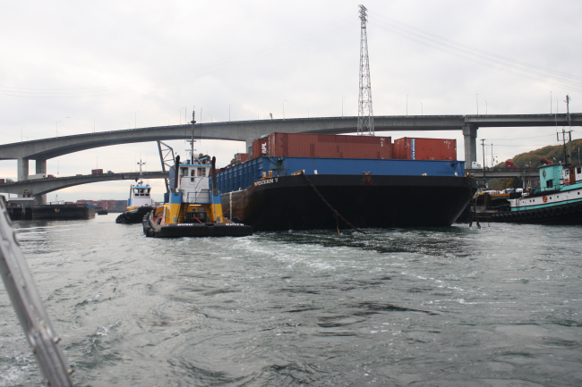 Container barge WESTERN 7 being maneuvered through narrow waterways