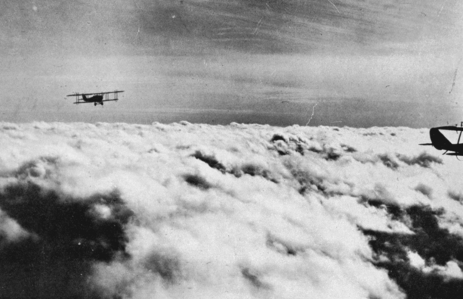 Military aircraft flying over layer of strato-cumulus; cirro-stratus above