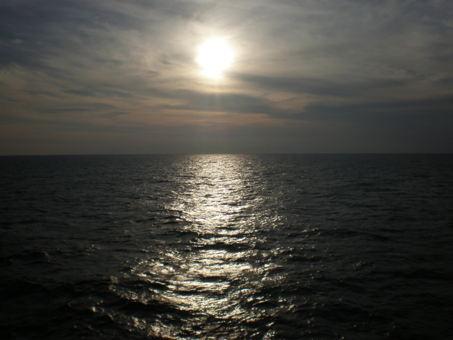 A gray colorless sunset with sunglint on the ocean surface