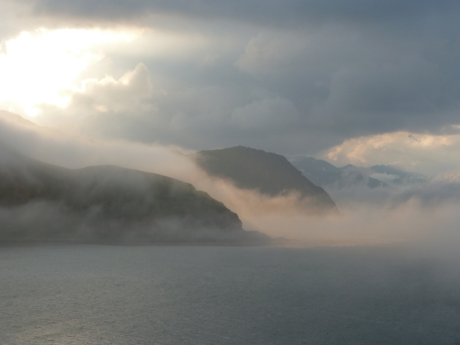 Early morning sun illuminating fog streaming off the mountains of Dutch Harbor