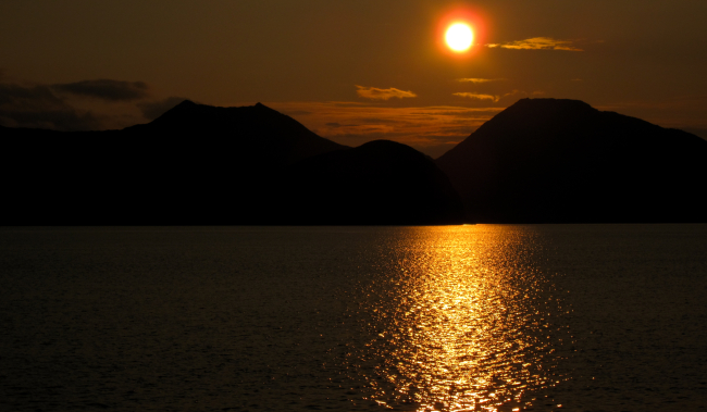 A bronze sun setting over the mountains and reflecting off the sea