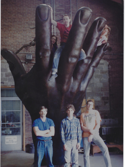 Raymond Kaskey stands in front of the NOAA hand, with two friends next to him and three more perched on the upstretched fingers of the large sculpture.