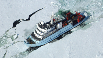 An aerial view of a large research ship cutting through sea ice.