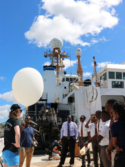 Scientists and Bajan students stand on the deck of the NOAA Ship Ronald H. Brown while examining an inflated weather balloon.