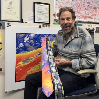Tim Schmit shows off two brightly patterned ties in front of a photo that matches one of them.