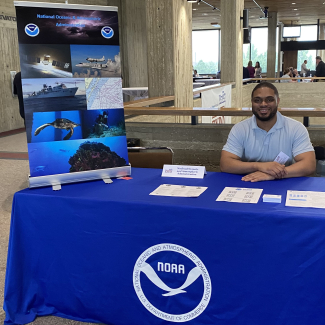 Photo of Blake Allen sitting behind a table at NOAA headquarters