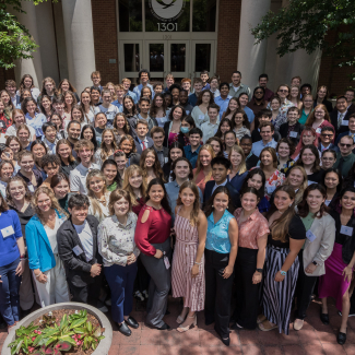 	A group photo of approximately 150 people young adults in business casual clothing. The group is posing outside in front a building with a NOAA logo on the door.