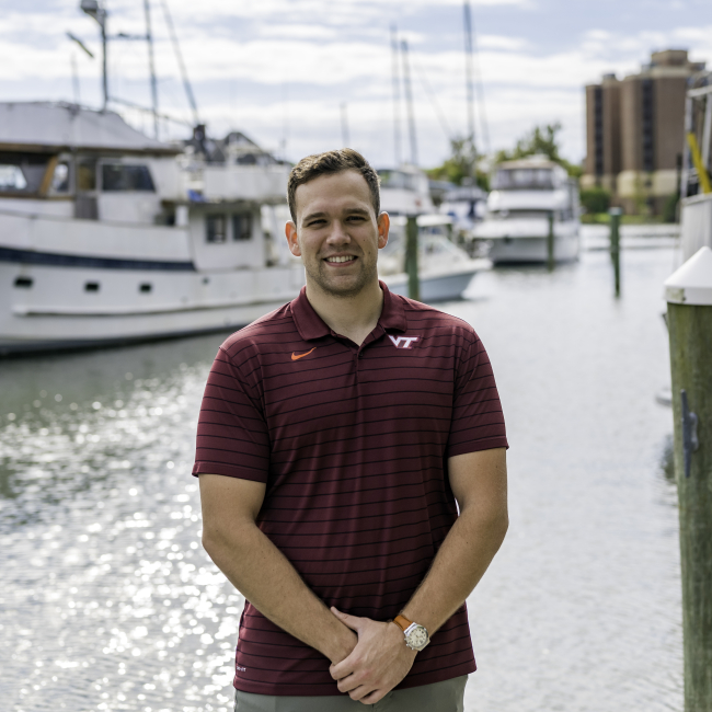 A person stands on a dock for a professional photo with boats behind them.