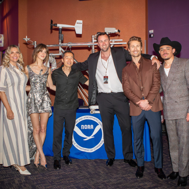 Twisters stars Glen Powell, Daisy Edgar-Jones and Anthony Ramos, along with director Lee Isaac Chung, pose in front of props from Twister during a tour of the National Weather Center and NOAA offices in Norman, Oklahoma in May, 2023.