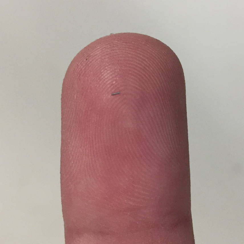 A close-up photo of a finger with a barely visible thin piece of metal resting on it.